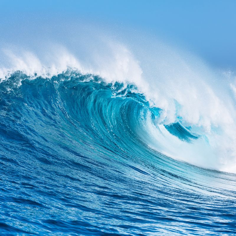 Powerful ocean wave curling over in bright blue water under a clear sky