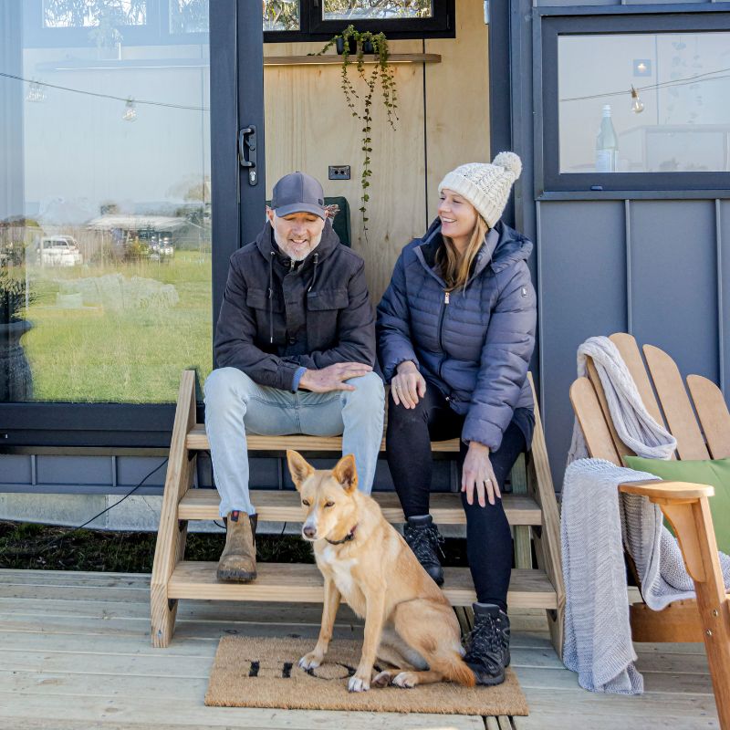 Tremayne Todd and Sarah Gole from Manuka Blue, sitting outside a small secondary home with their Kelpie, Tash.